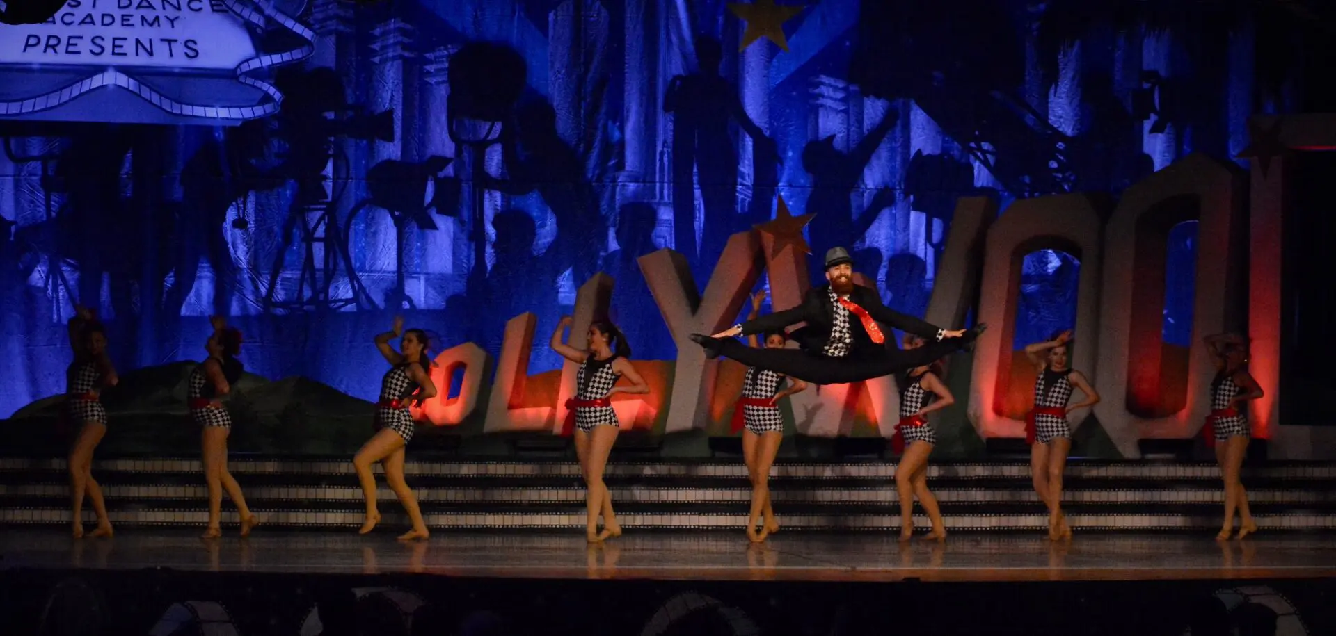 A group of dancers performing on stage in front of a large sign.